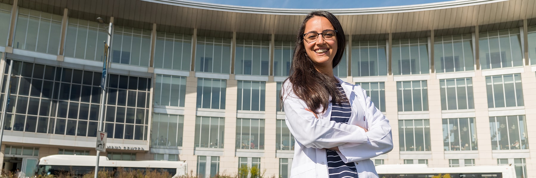 Student in lab coat poses in front of the Campus Center.