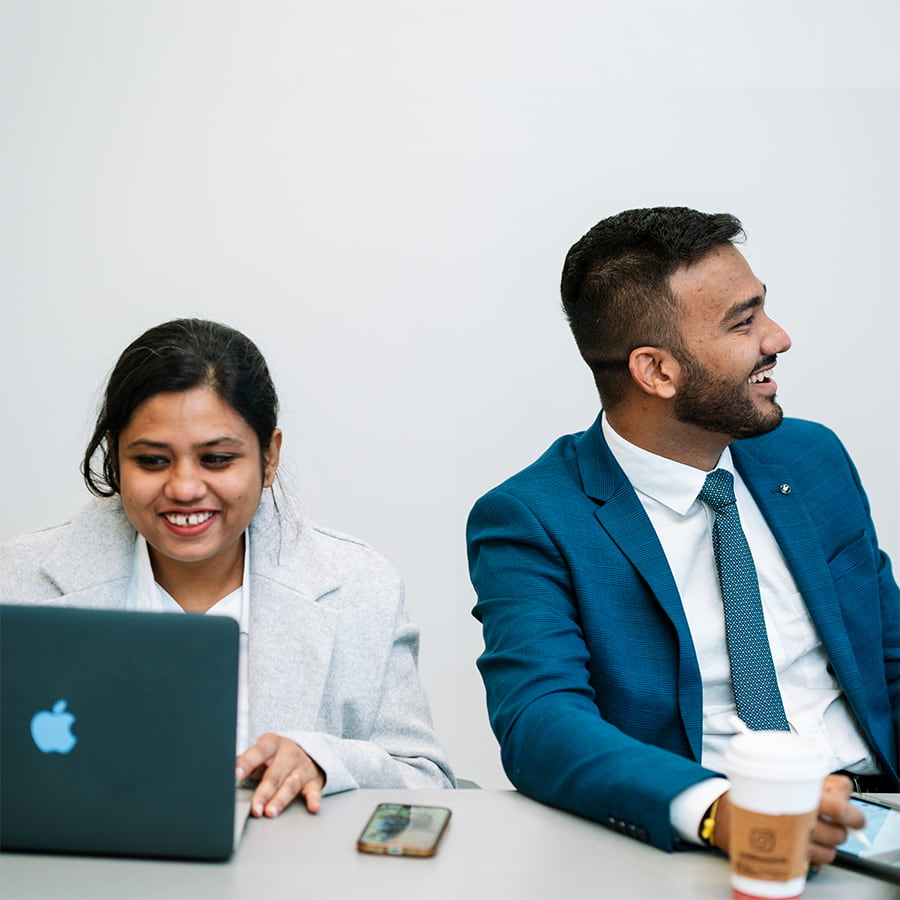 Graduate students smiling while sitting at table and taking notes with laptops and tablets.