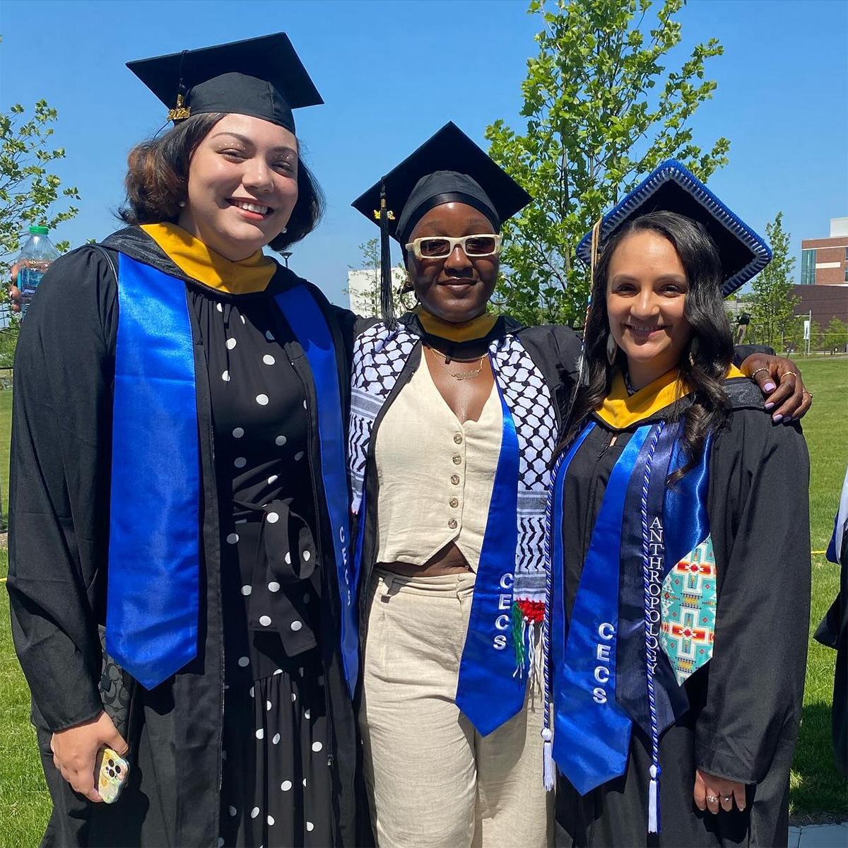 Three graduates of the Critical Ethnic and Community Studies program smile in their commencement robes