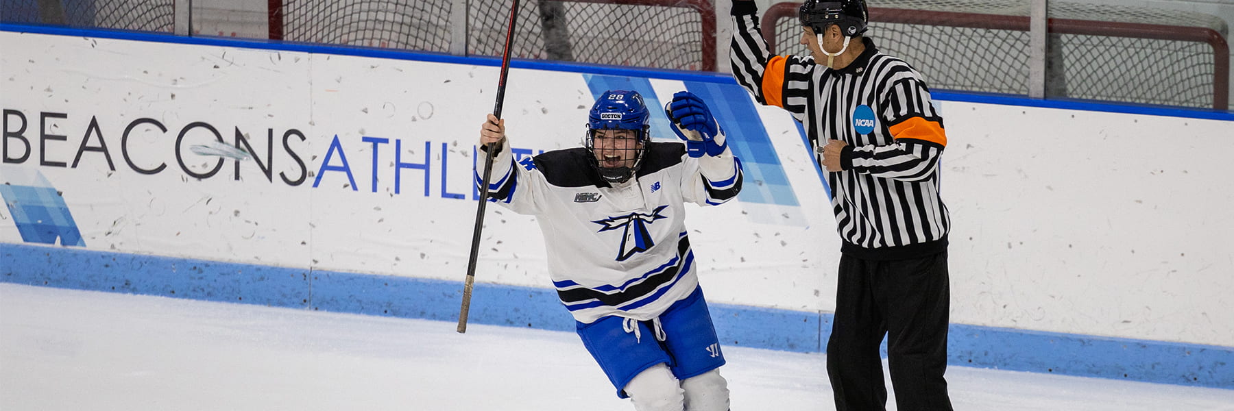 Female hockey player in rink in uniform raises hands and stick in triumph.