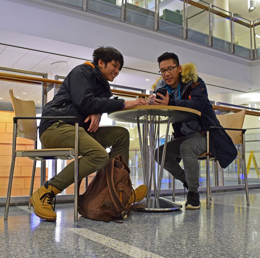Two students are on their phones and interacting in ISC