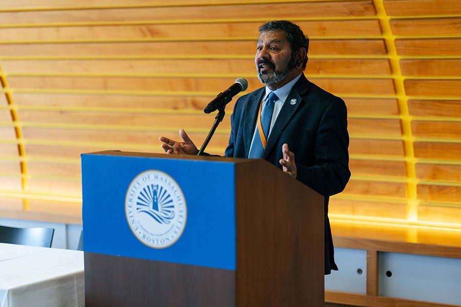Bala Sundaram speaks at a podium in front of a wooden wall.