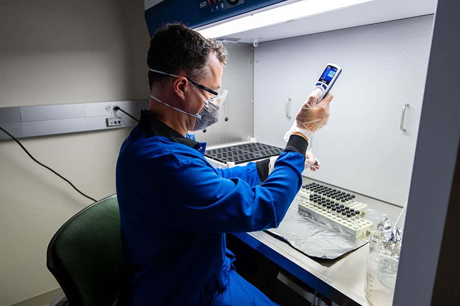 Jesse Farmer, wearing a mask and gloves, holds a pipette under a hood in his lab