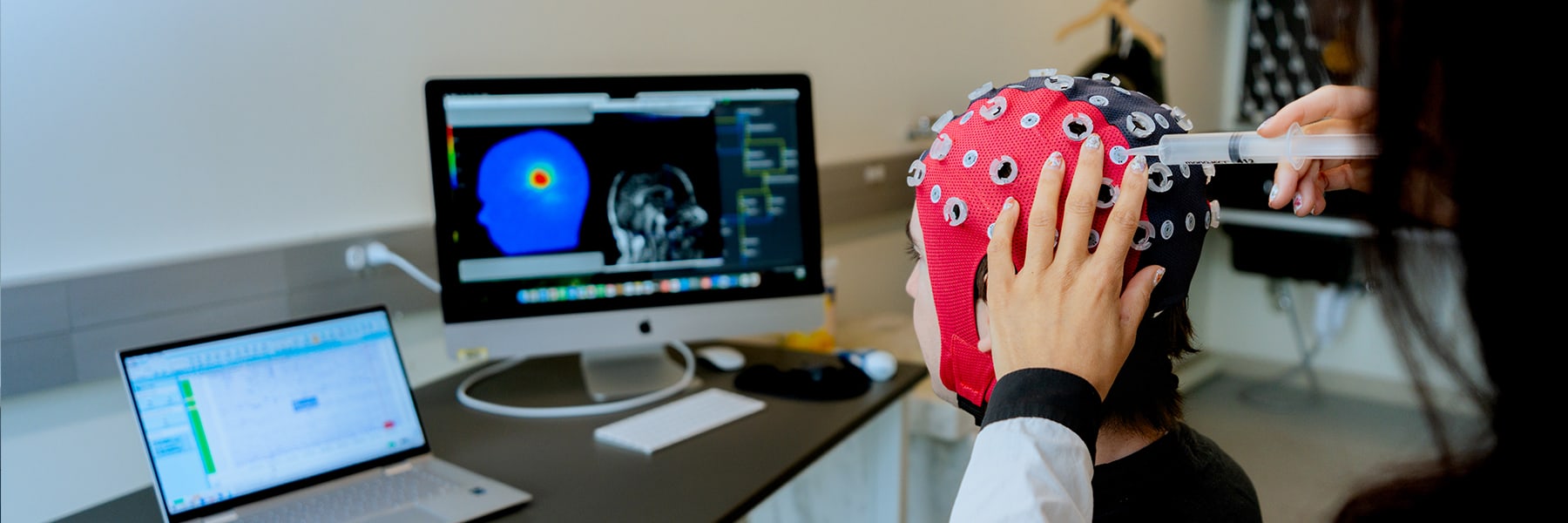 professor works with student wearing cap with brain sensors in lab.