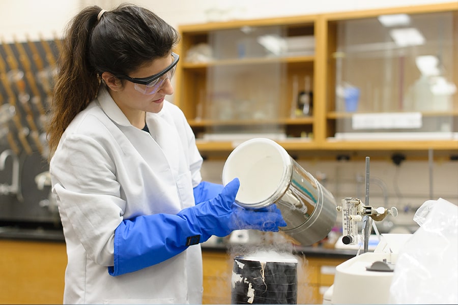 female student in goggles & gloves works in lab.
